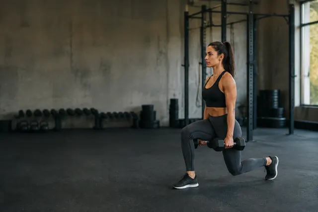 A woman doing a dumbbell lunge in a bright, quiet room