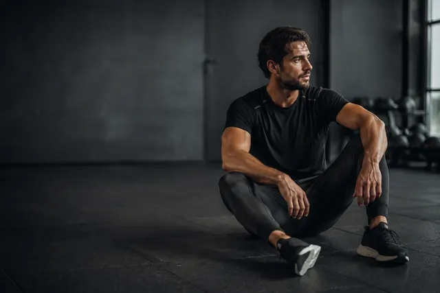 A man sitting on a gym floor resting between sets